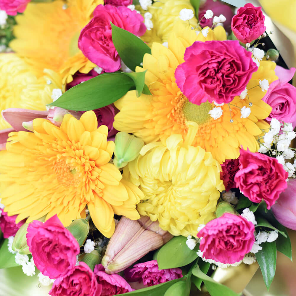 Exotic Eden Mixed Floral Bouquet. Mini carnations, tulips, roses, lilies, chrysanthemums, baby's breath, ruscsus in shades of pink and yellow, gathered in a floral wrap tied with designer ribbon. Mixed Floral Gifts from Monthly Sommelier USA - Same Day USA Delivery.